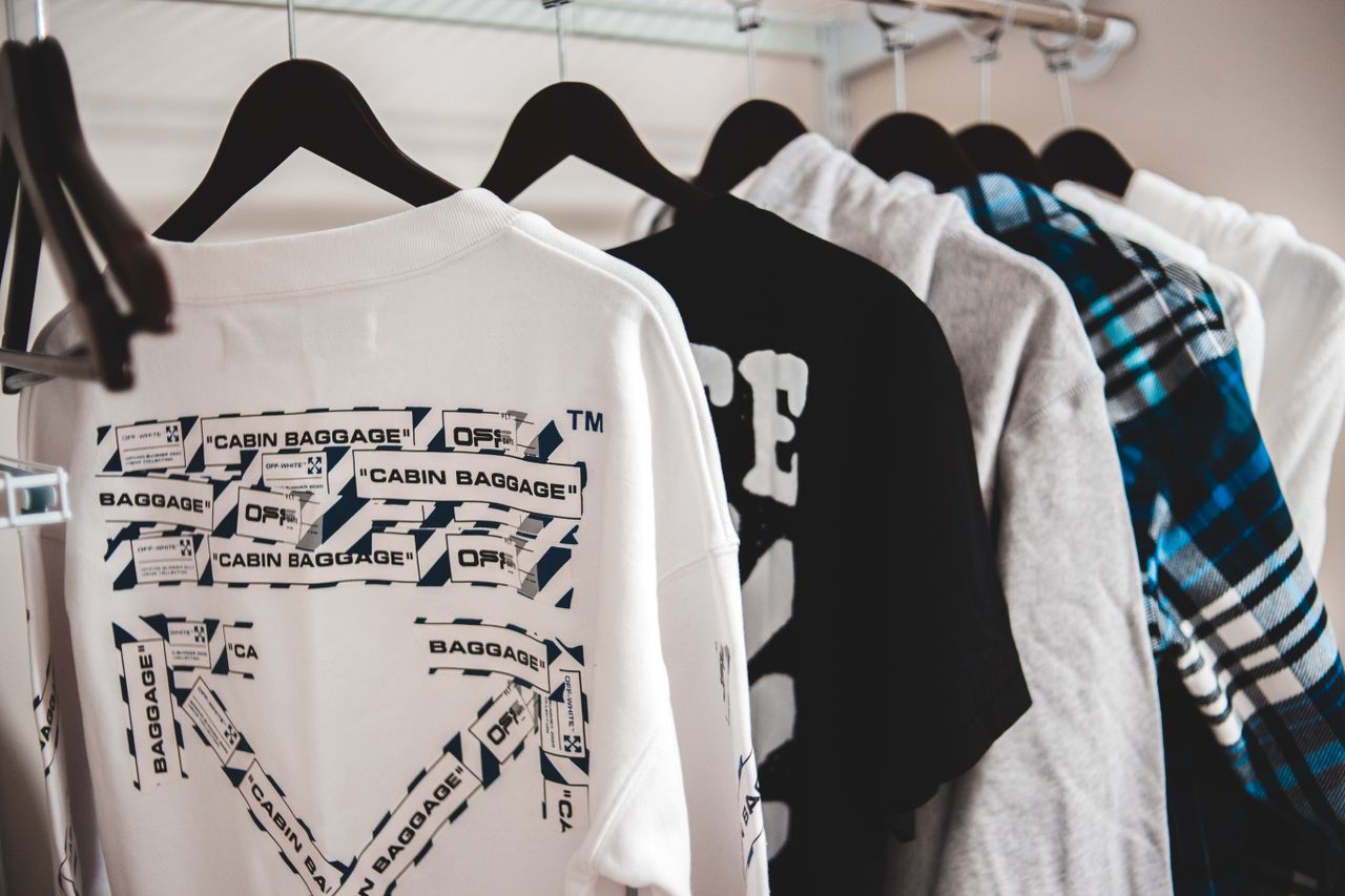 Assorted stylish male apparel hanging on plastic racks on metal beam in wardrobe